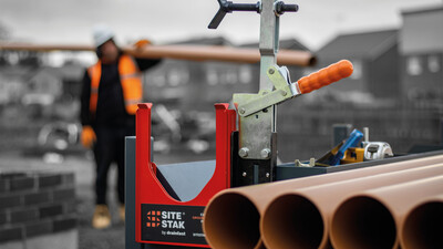 Construction worker carrying a length of drainage pipe to a SiteStak workstation to cut it